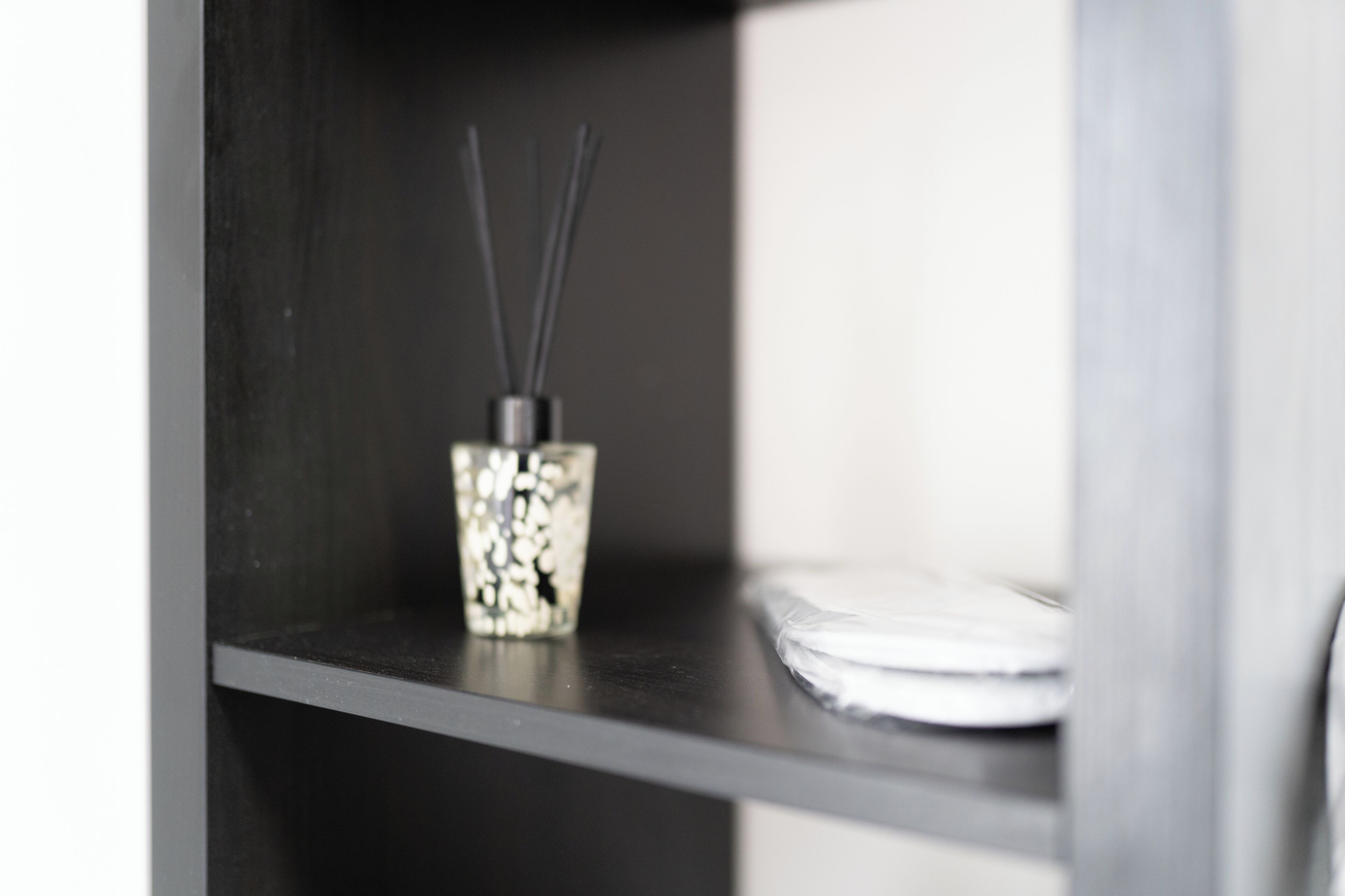 A shelf with a decorative container holding reed diffusers and a stack of white plates.