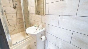 A modern bathroom with a glass-enclosed shower, a white sink with a mirror, and light-colored tiles.