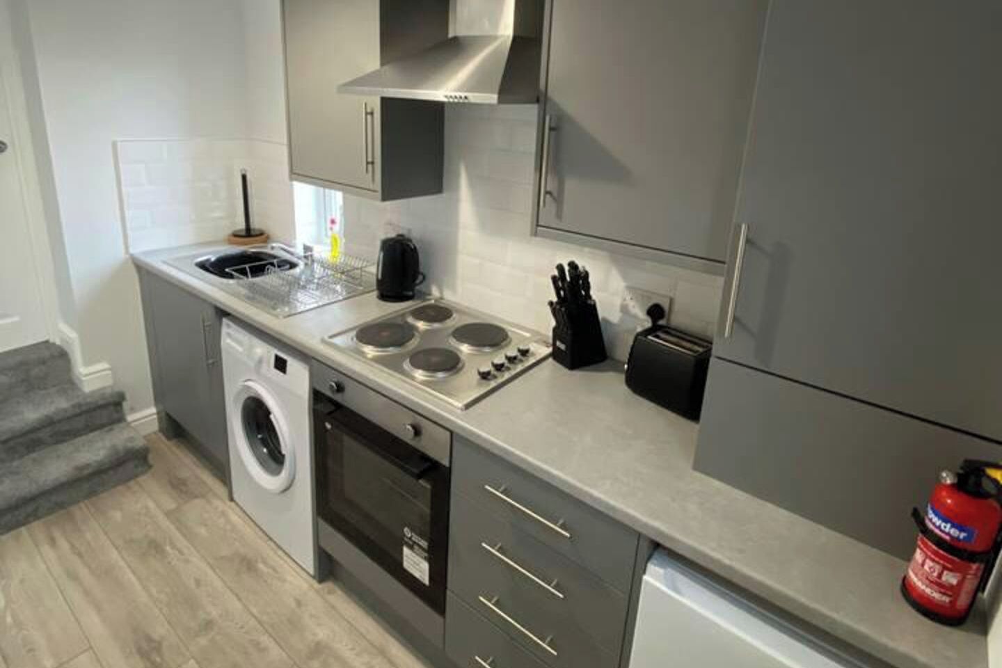 Een kleine keuken met een wasmachine, kookplaat en broodrooster.