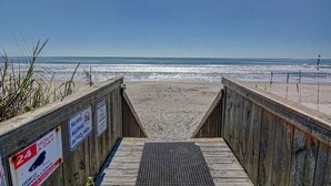 Ein hölzerner Steg führt zu einem Strand, auf dem Schilder darauf hinweisen, dass keine Haustiere erlaubt sind und ein Überwachungssystem rund um die Uhr in Betrieb ist.