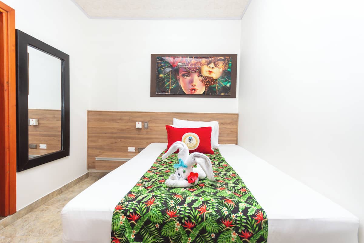 A hotel room with a bed, a painting on the wall, and a window.