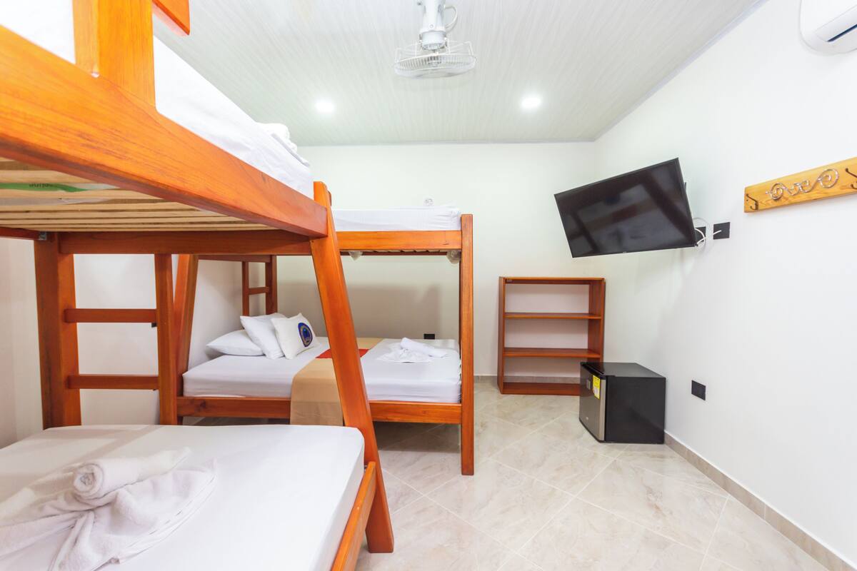 A room with bunk beds, a television mounted on the wall, and a small wooden shelf.