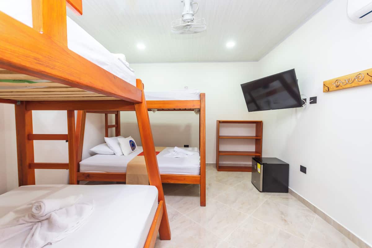 Una habitación con literas, un televisor montado en la pared y un pequeño estante de madera.