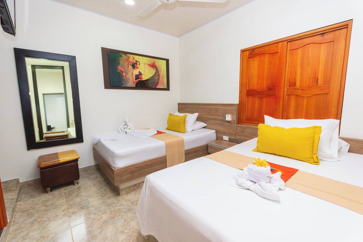 A hotel room with two beds, a wooden headboard, a painting on the wall, a mirror, and a small wooden bench.