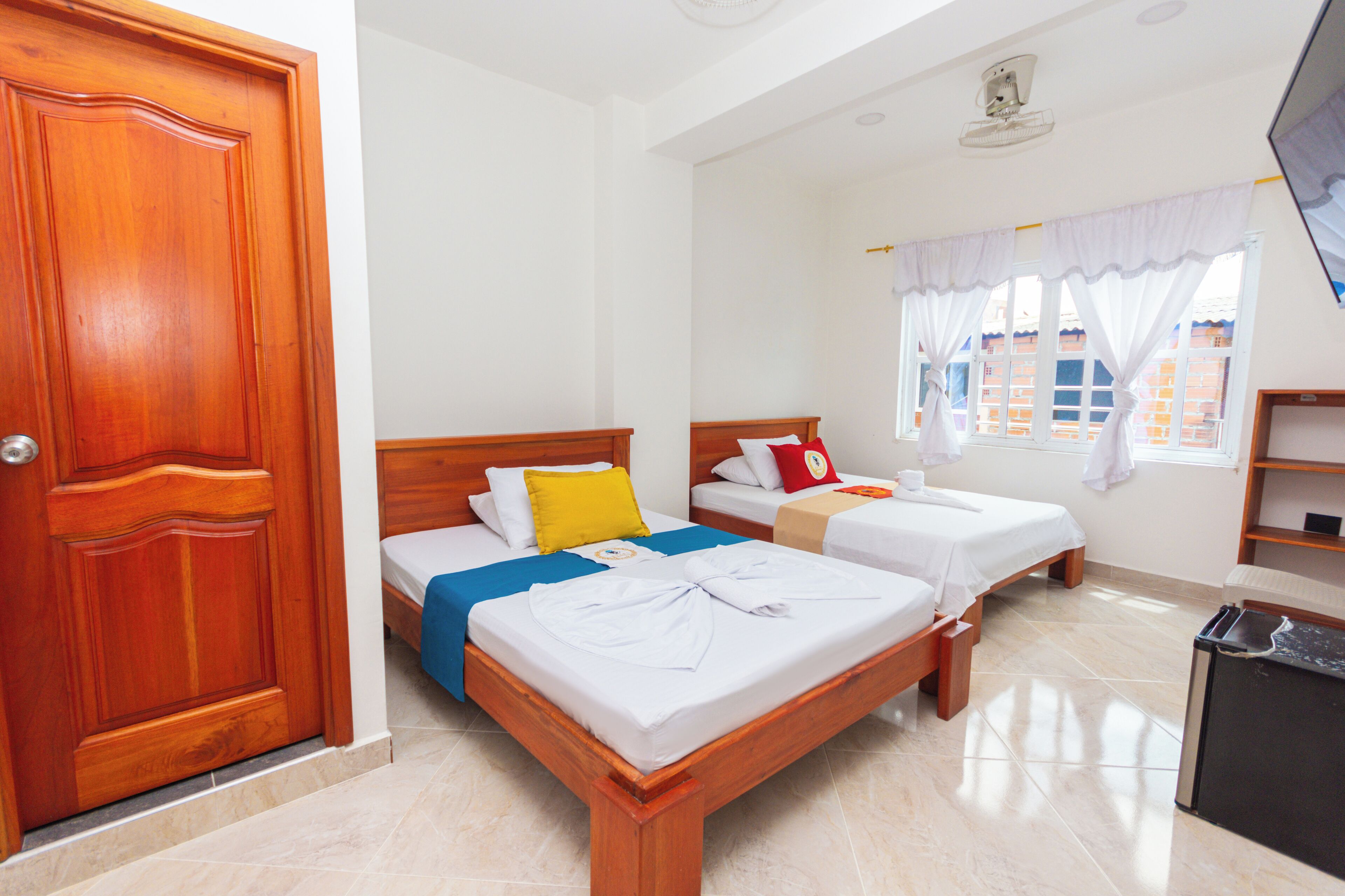 A hotel room with two beds, a wooden door, a small desk, and a window with curtains.
