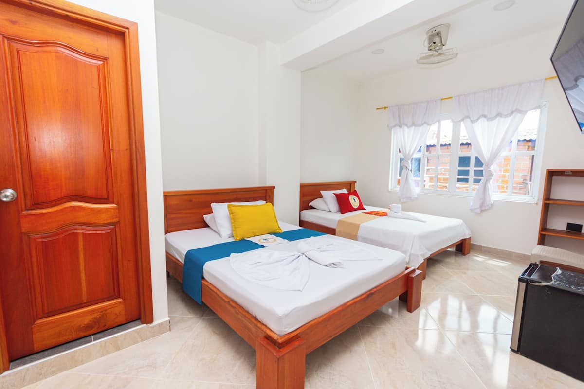 Habitación de hotel con dos camas, una puerta de madera, un escritorio pequeño y una ventana con cortinas.