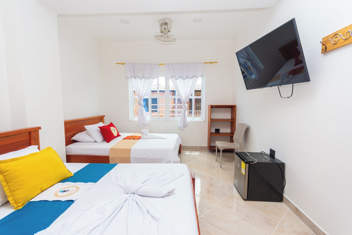 Une chambre d’hôtel avec deux lits, une télévision, un bureau et une fenêtre avec des rideaux.
