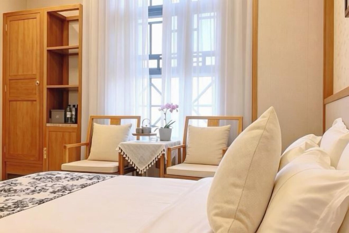 Habitació d'hotel amb un llit, dues cadires, una taula petita amb un ram i un armari de fusta.