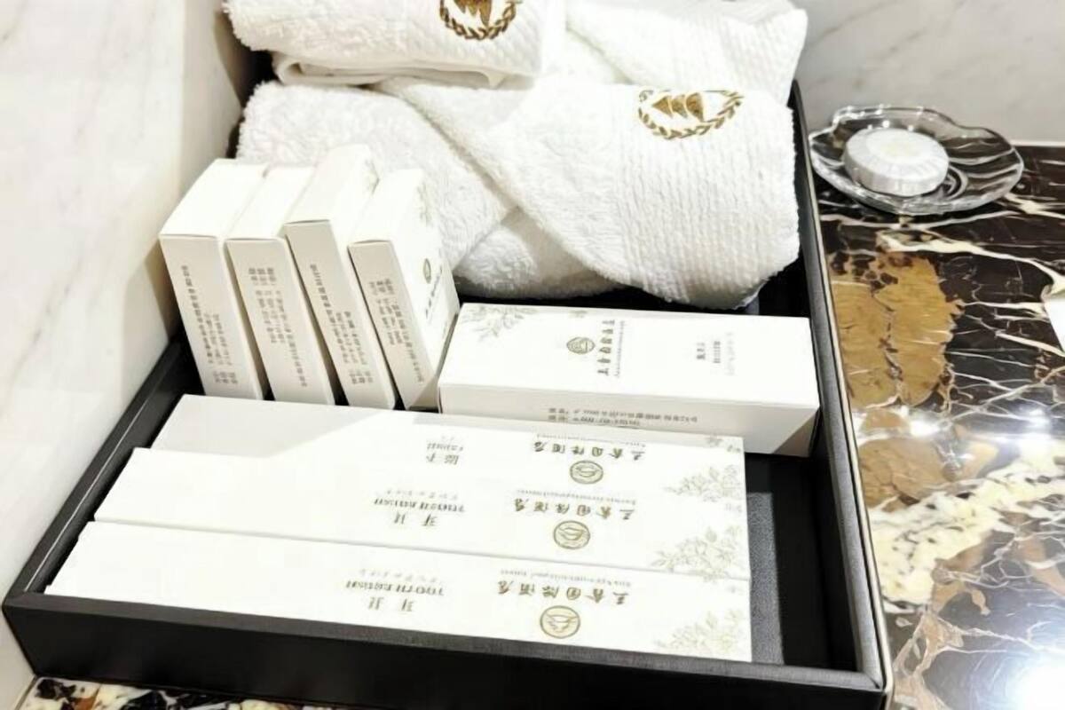 Una caja de toallas blancas con bordado dorado y una bandeja de toallas blancas sobre una superficie de mármol.