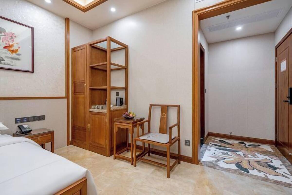 Una habitación de hotel con una cama, un armario de madera, una mesita con una silla y un diseño decorativo en el suelo.
