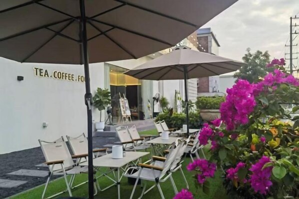 Un área de estar al aire libre con mesas y sillas, sombrillas y un cartel que dice 'TEA COFFEE'.