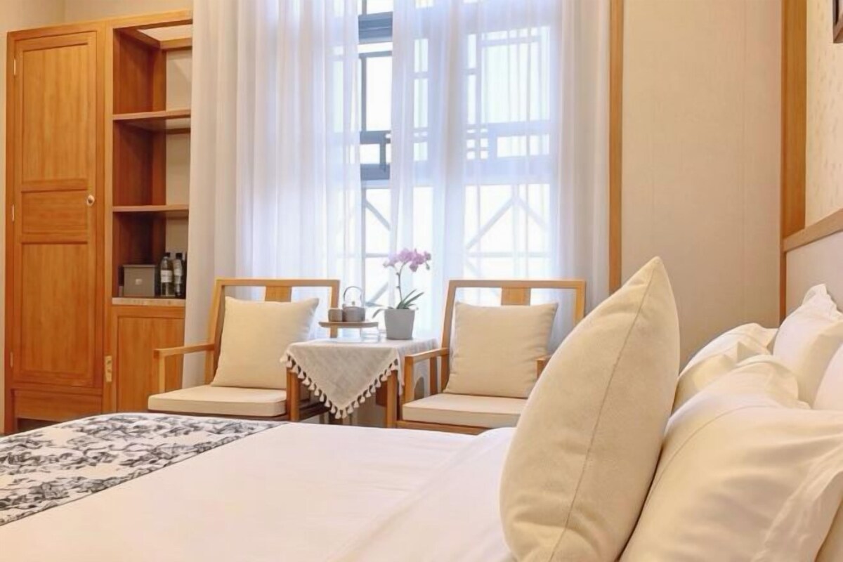Ein Hotelzimmer mit einem Bett, zwei Stühlen, einem kleinen Tisch mit Blumenvase und einem Kleiderschrank.