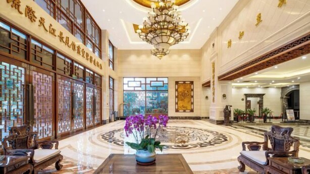 Un hall espacioso con decoración tradicional, un candelabro y un arreglo floral central.