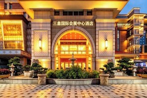 Entrada de hotel con un arco, una fuente y un jardín cuidado.