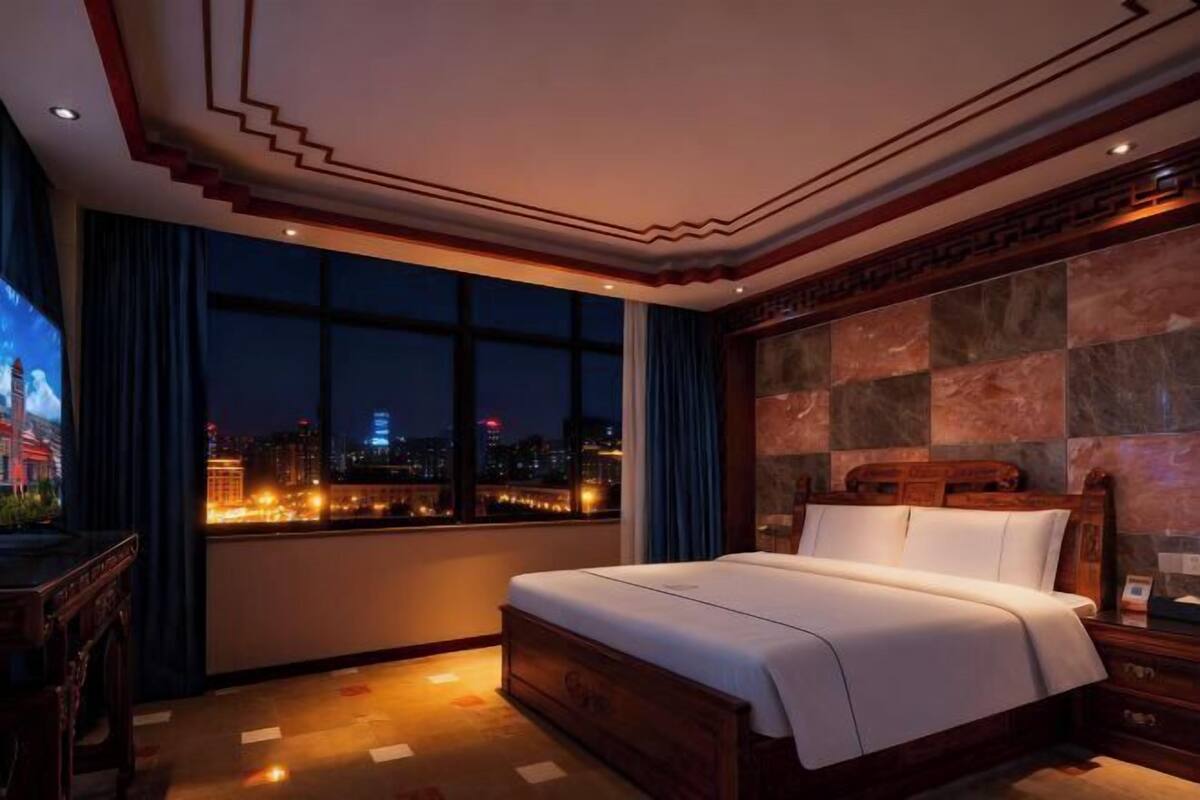 A hotel room with a large bed, a night view of the city, and a decorative ceiling.
