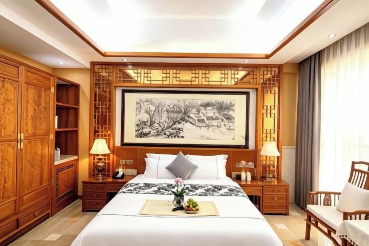 A hotel room with a large bed, wooden furniture, a painting on the wall, and a desk with a lamp.