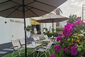 Een terras met tafels en stoelen, parasols en een gebouwde ingang op de achtergrond.