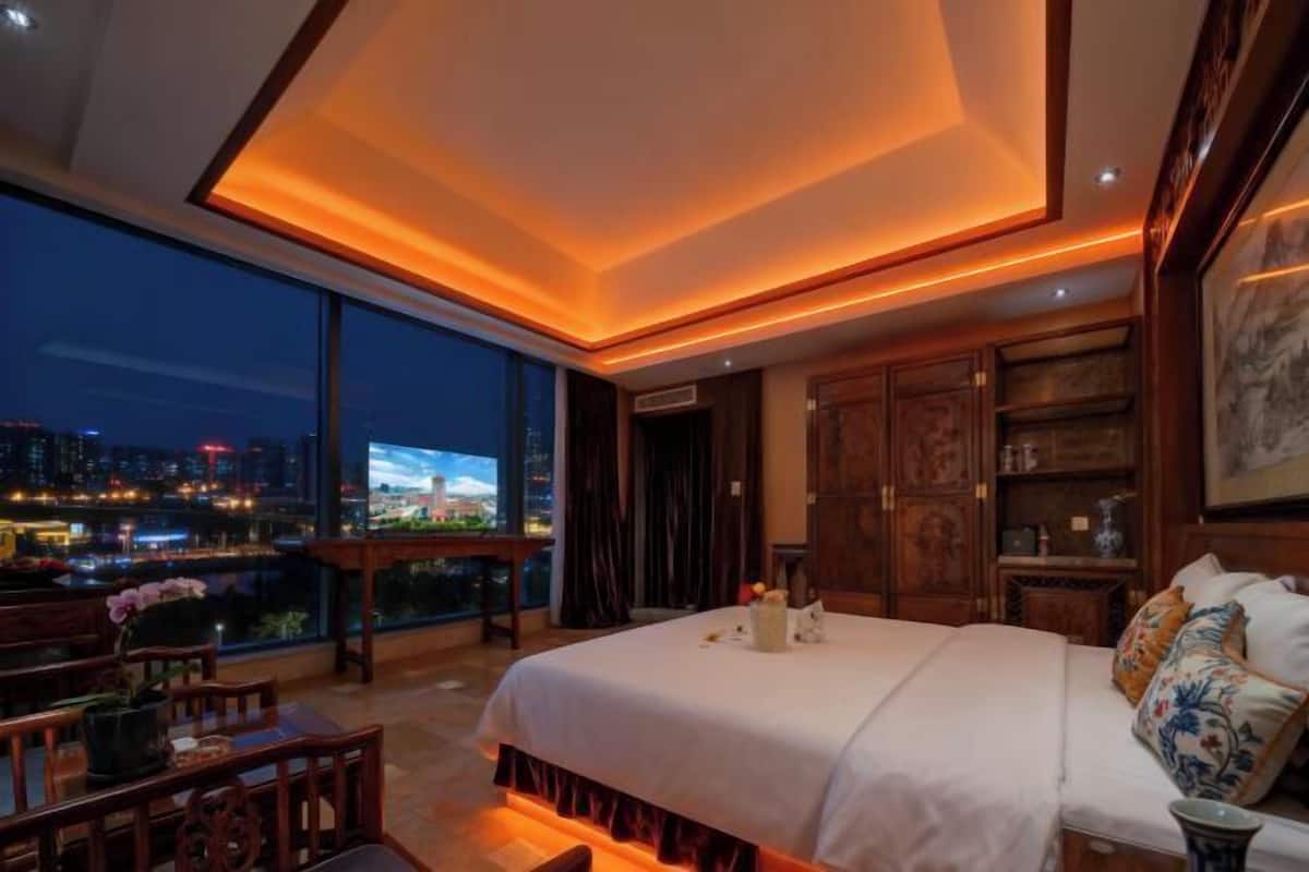 Habitación de hotel moderna con una cama grande, muebles de madera, vistas a la ciudad y un balcón.