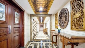 Un pasillo con suelo de mármol a cuadros, puertas de madera y techo con diseño geométrico.