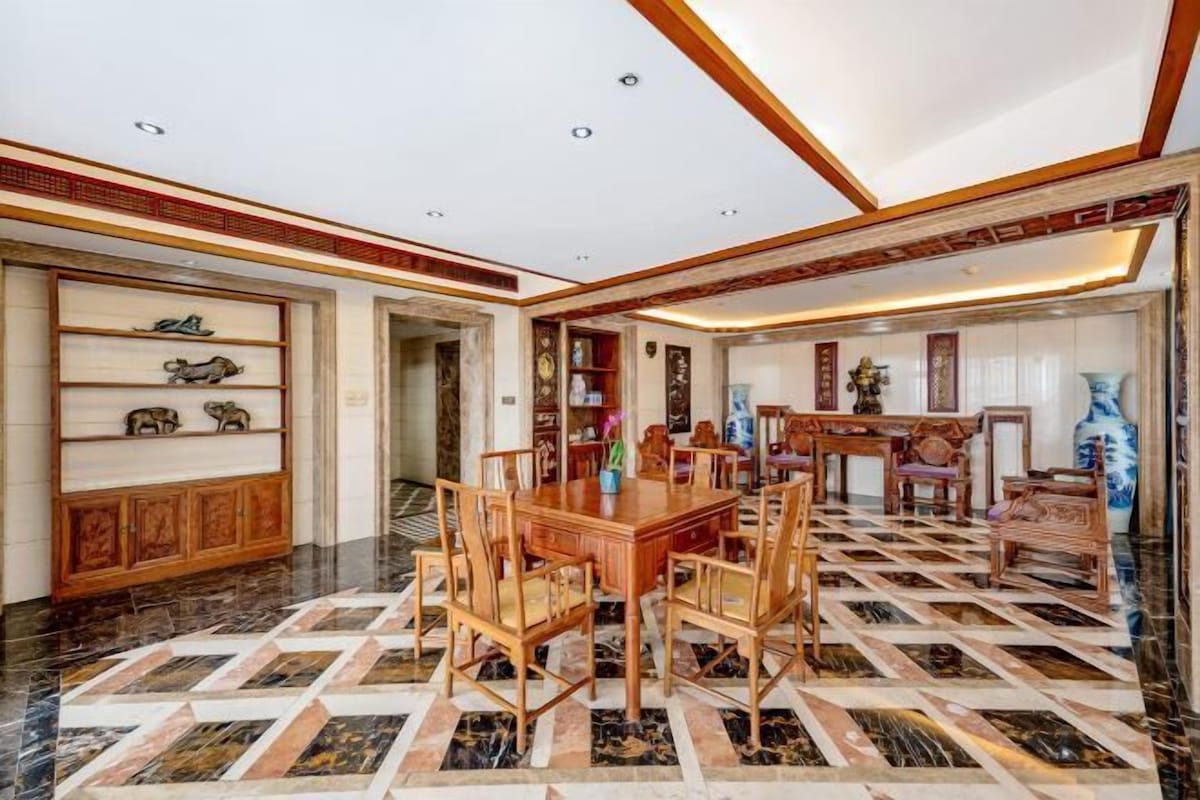 A spacious room with a large wooden dining table surrounded by chairs, a patterned floor, and traditional decor.