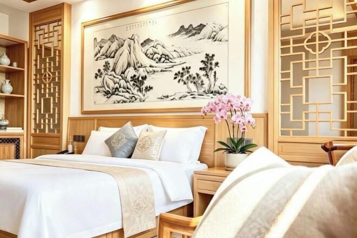 A traditional-style bedroom with a large bed, bedside tables, a decorative screen, and a framed artwork on the wall.