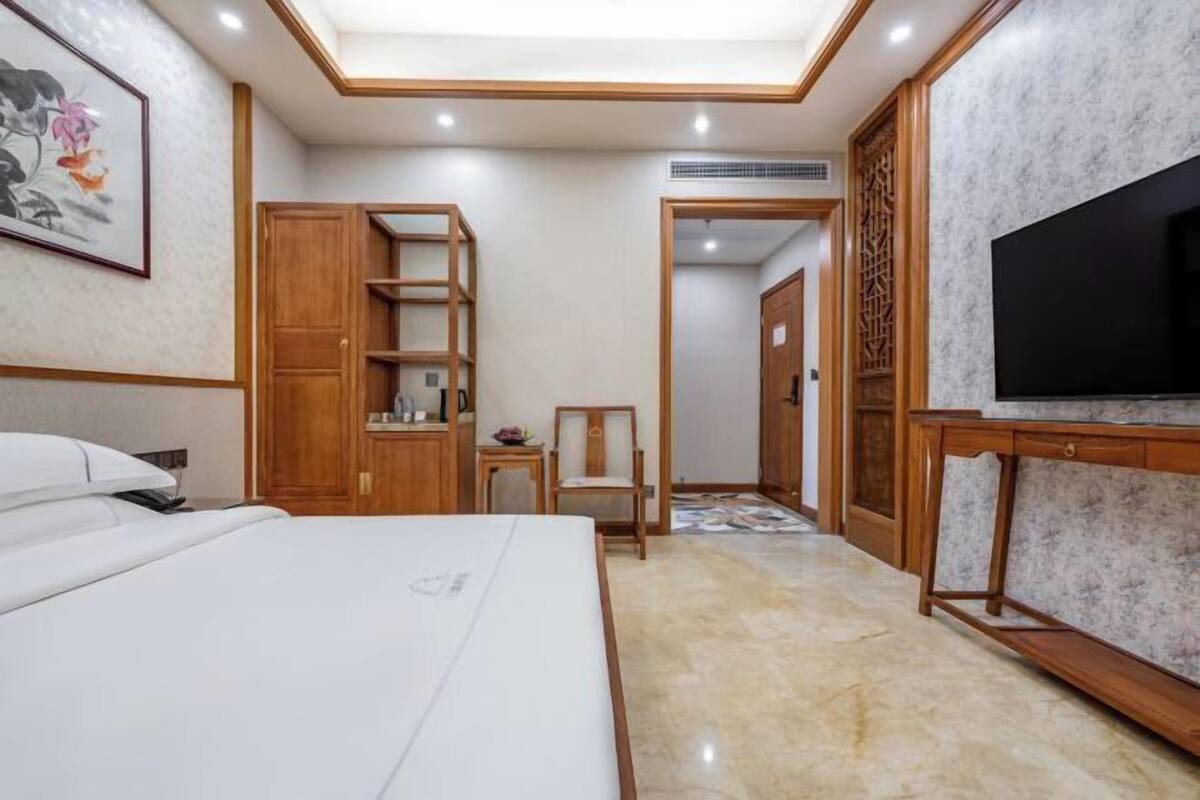 A hotel room with a bed, a TV, a wooden wardrobe, and a small table.