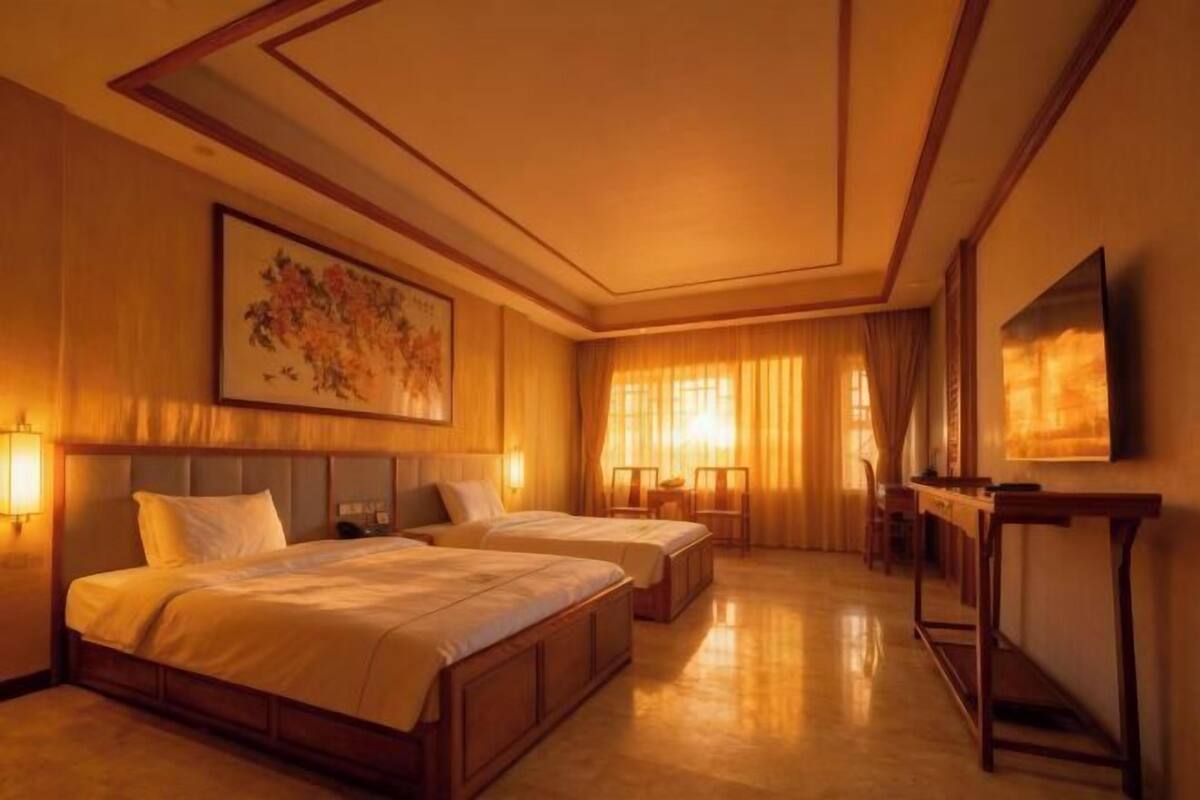 A hotel room with two beds, a desk, a chair, and a TV.