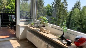 Een moderne kamer met een groot raam, een radiator, een bank en uitzicht op bomen.