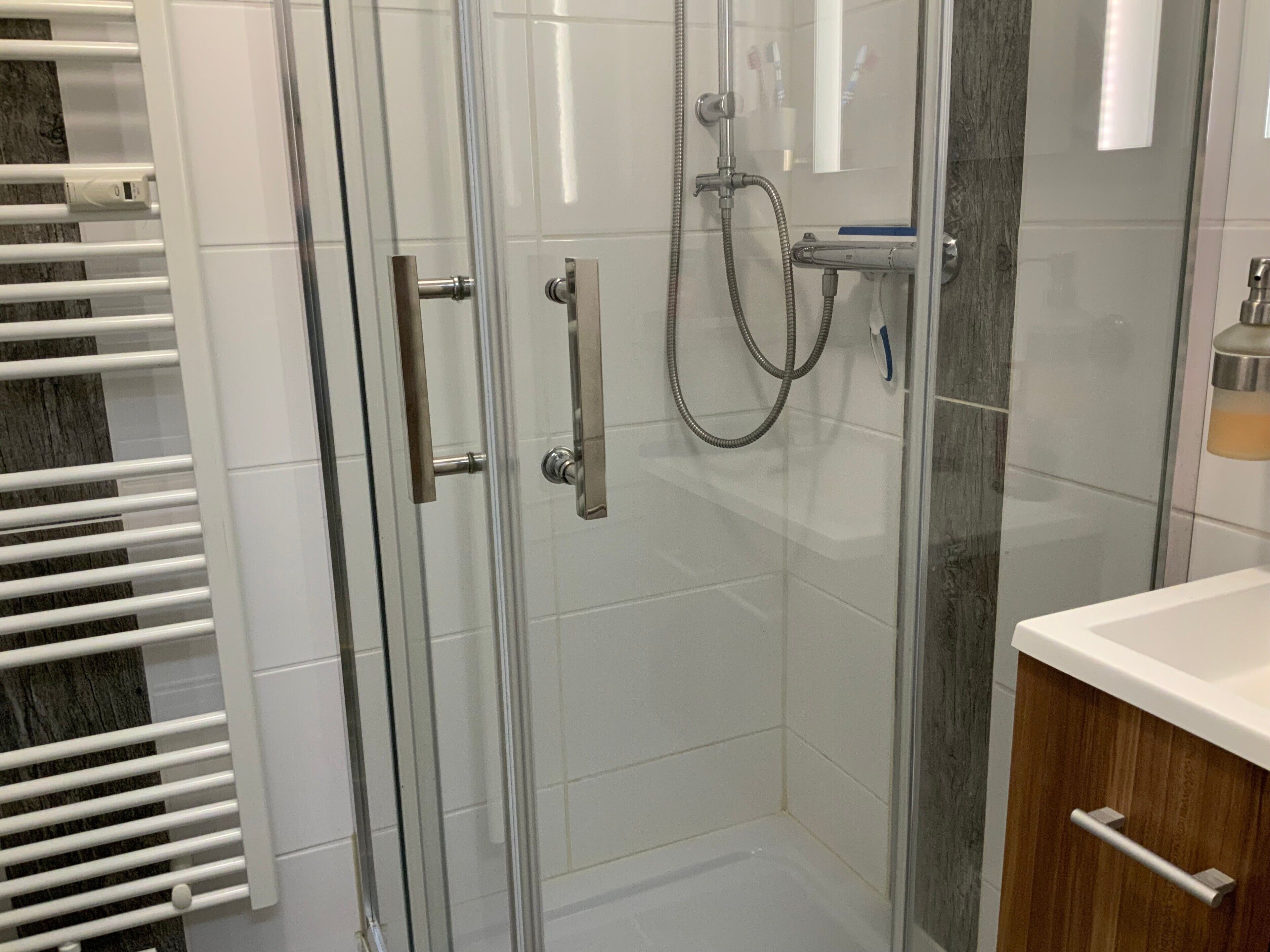 A glass-enclosed shower with a handheld showerhead, a towel rack, and a wooden cabinet with a drawer.