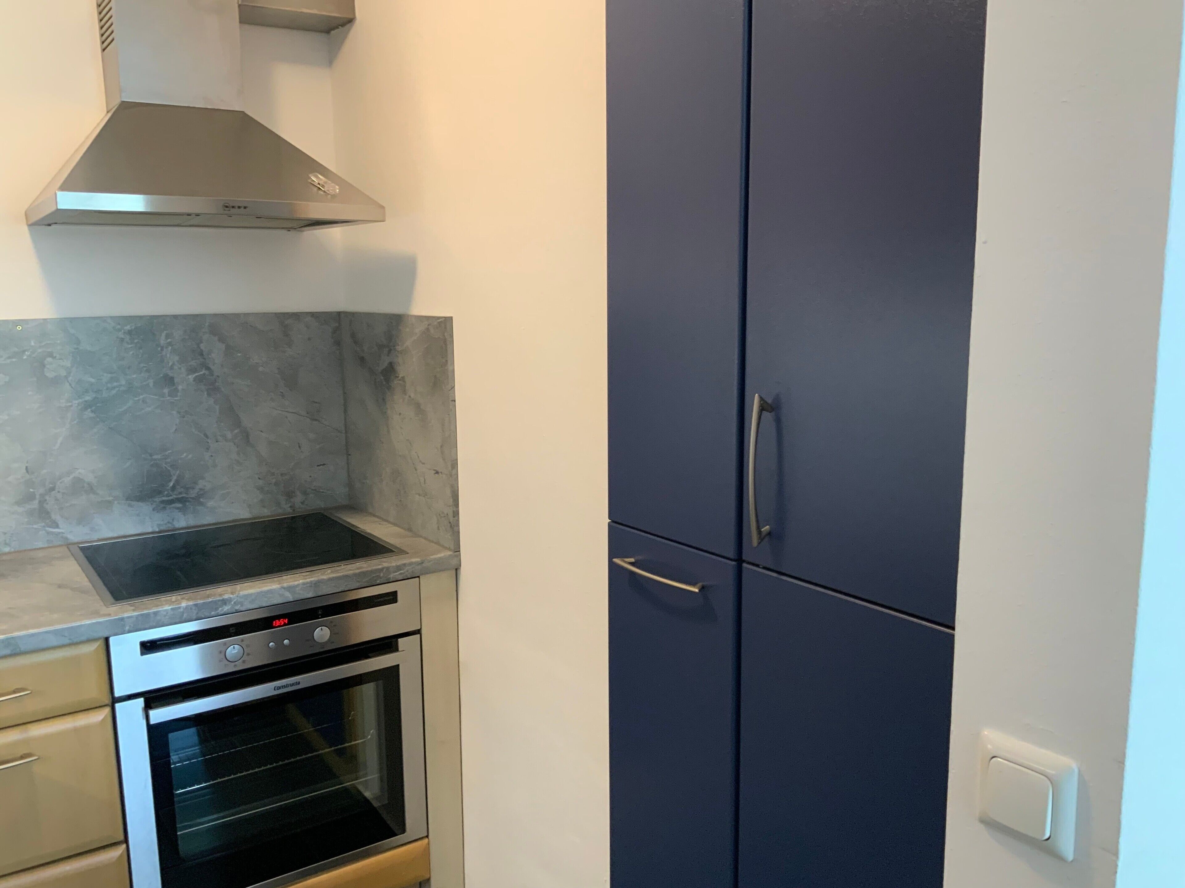 Una cocina con horno empotrado, campana extractora de acero inoxidable y un armario azul oscuro.