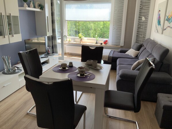 Un salon moderne avec un coin repas, comprenant un ensemble de canapés, un téléviseur et une table à manger avec des sets de table.