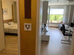 Une pièce comprenant un lit, un bureau et une chaise. Il y a une fenêtre donnant sur un paysage verdoyant.