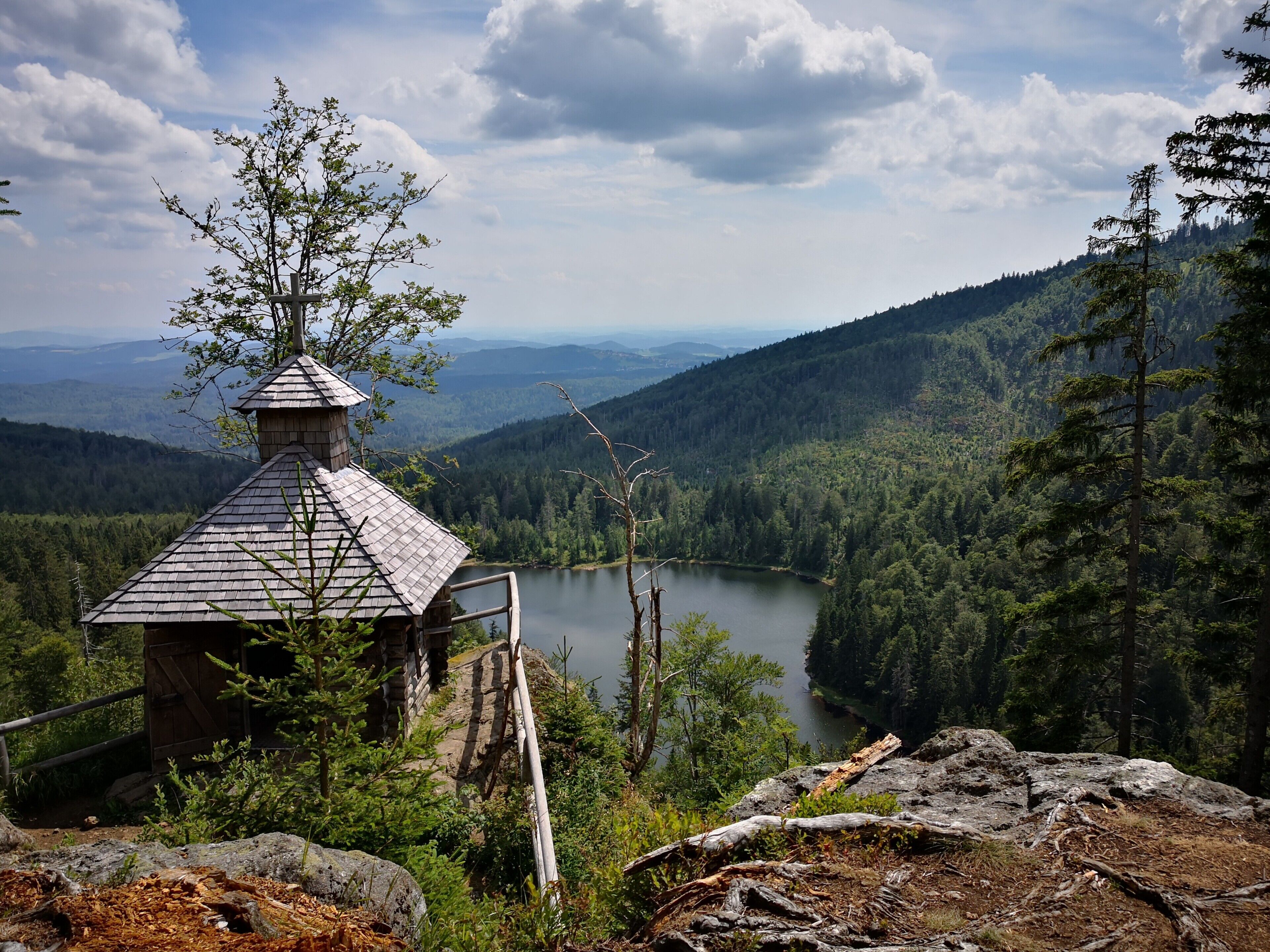 Una baita con tetto spiovente, una scala in legno e vista su un lago circondato da colline boschive.