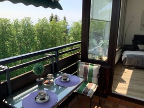 Un balcon avec une table dressée pour deux personnes, une petite plante en pot et une vue sur une zone boisée.
