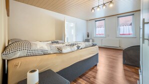 A bedroom with a bed, a wooden floor, a ceiling light fixture, and windows with curtains. - Holiday Apartment "Bartölke" with Wi-Fi (Bockenem)