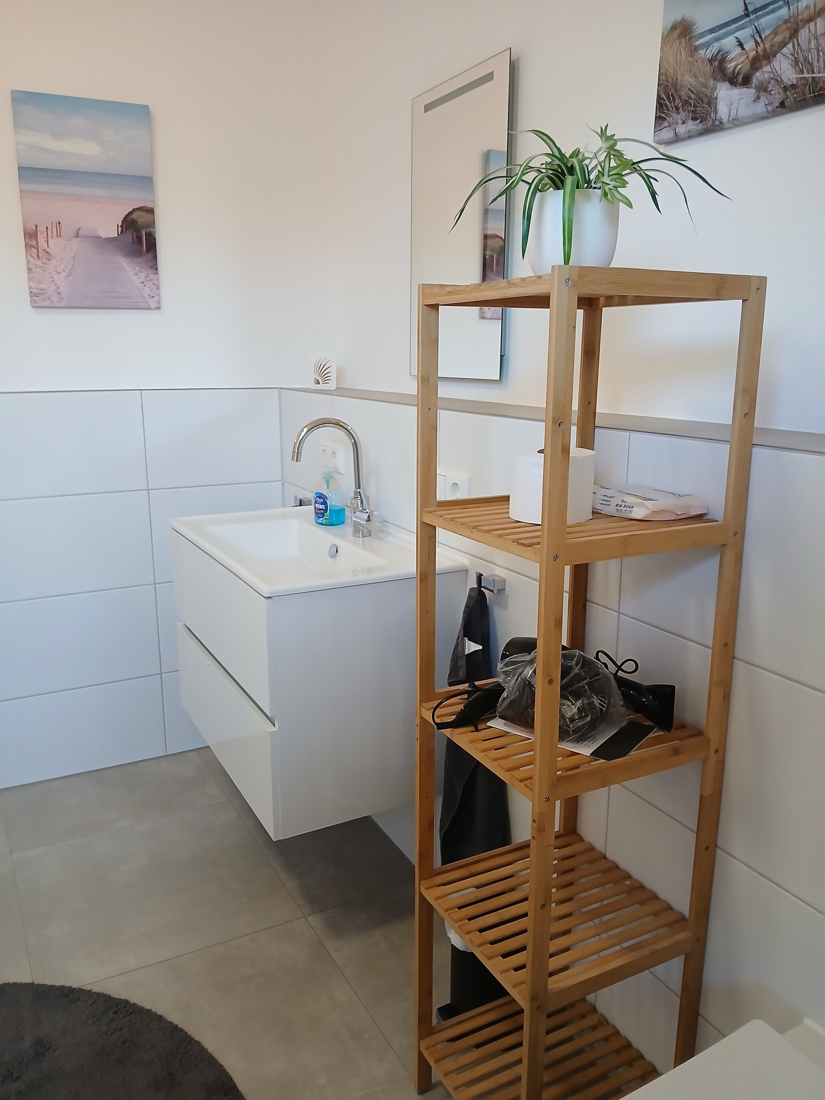 Ein Badezimmer mit einem weißen Waschbecken, einem Holzregal mit einer Topfpflanze und einem Handtuchhalter.