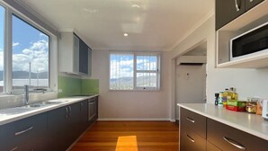 A modern kitchen with a large window, wooden flooring, and built-in appliances. - The Mountain Riveting House at Risdon vale (Risdon Vale)
