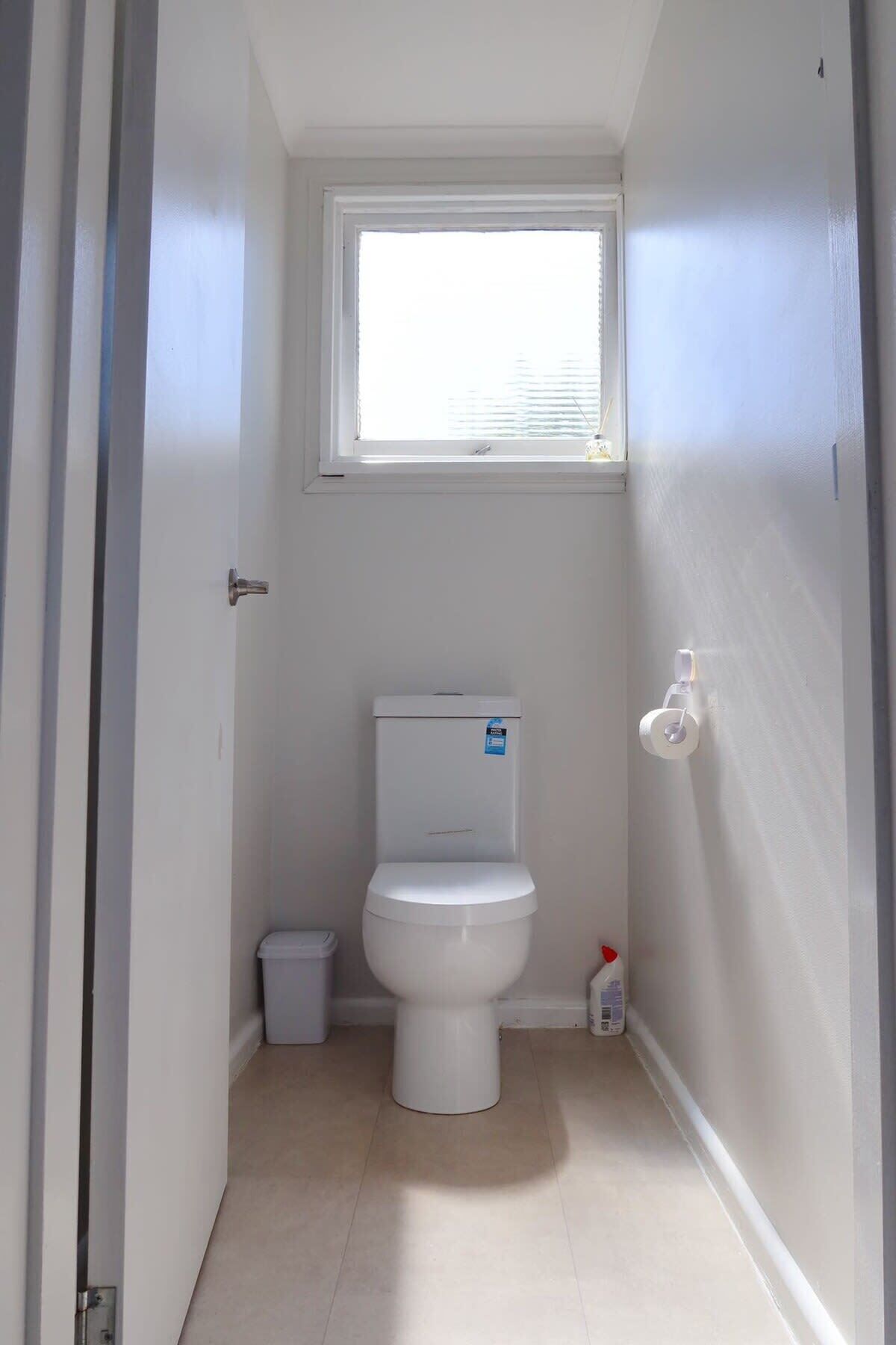 A small, narrow bathroom with a toilet, a window, and a white door.