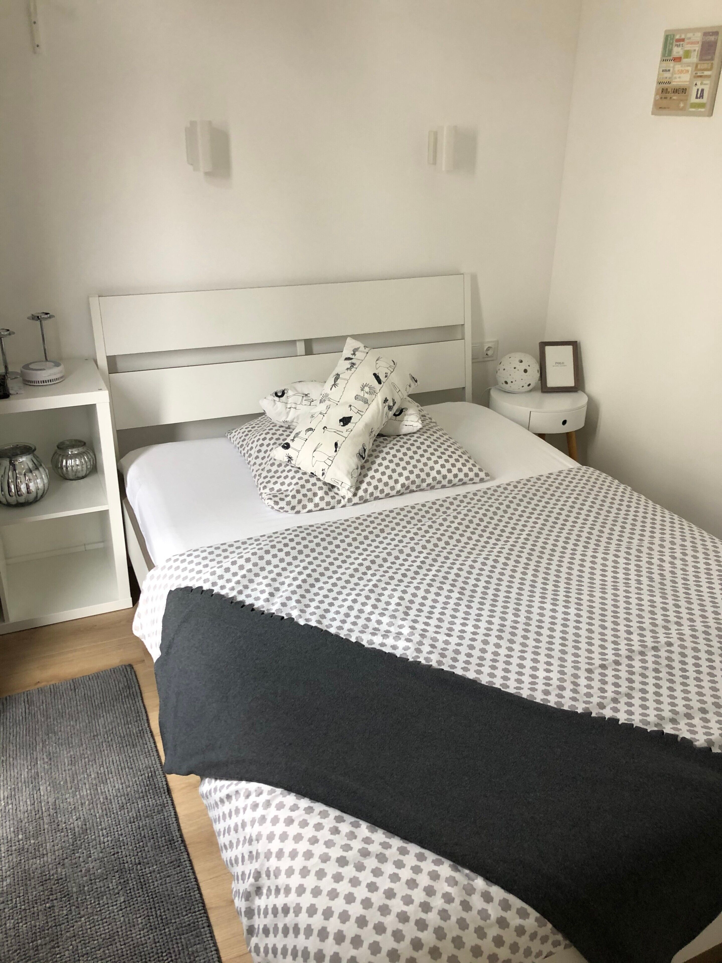 Une chambre à coucher bien rangée, avec un lit, des oreillers, une table de chevet et une étagère fixée au mur.