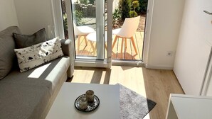 Ein Wohnzimmer mit einer Couch, einem Couchtisch und einer Glasschiebetür, die auf eine Terrassenanlage mit einem Stuhl und einem kleinen Tisch führt.
