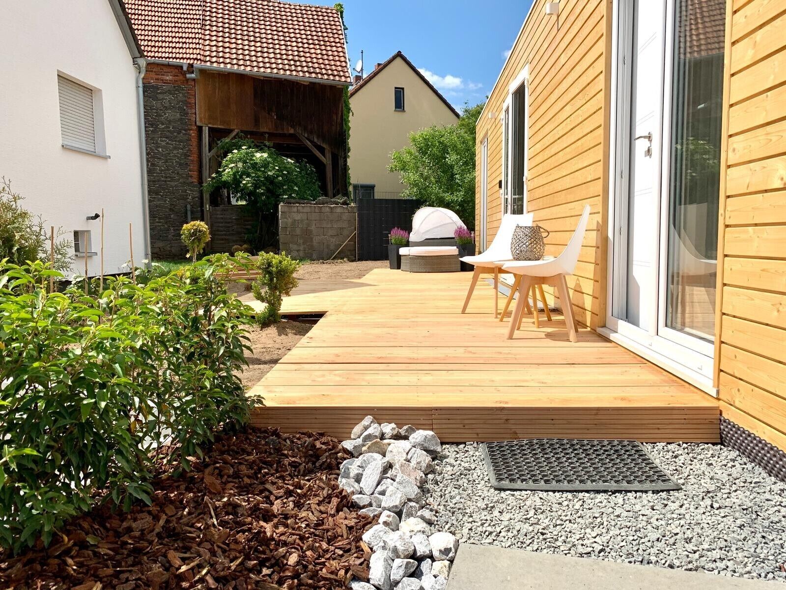 A wooden deck with outdoor seating, a stone pathway, and a small garden area.