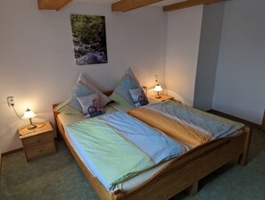 Une chambre à coucher avec un lit en bois, deux tables de chevet avec des lampes, un tableau accroché au mur et une petite commode.