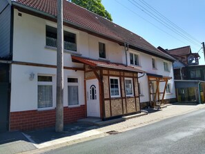 Un bâtiment à deux étages de style architectural traditionnel, doté d’un balcon, d’un porche en bois et d’une porte d’entrée bien visible.