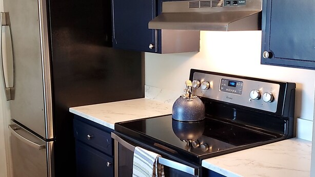 A kitchen with dark cabinets, a stainless steel refrigerator, a stove, and a microwave. - Welcome to Casa de Cruz where everything is a short drive away! Perfect for you! (Tampa)
