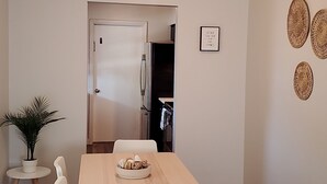 A dining area with a wooden table and white chairs, a potted plant, and a kitchen in the background. - Welcome to Casa de Cruz where everything is a short drive away! Perfect for you! (Tampa)