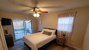 A bedroom with a bed, a ceiling fan, a TV mounted on the wall, and a sliding glass door leading to an outdoor area. - Welcome to Casa de Cruz where everything is a short drive away! Perfect for you! (Tampa)