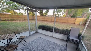 A covered patio with a patterned rug, wooden furniture, and a view of a backyard with a wooden fence and trees. - Welcome to Casa de Cruz where everything is a short drive away! Perfect for you! (Tampa)
