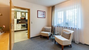 A hotel room with a kitchenette, a dining area with a table and two chairs, a large window with sheer curtains, and a framed picture on the wall. - Apartment "Am Kapellenberg" with Mountain View, Shared Terrace & Wi-Fi (Bad Peterstal-Griesbach)