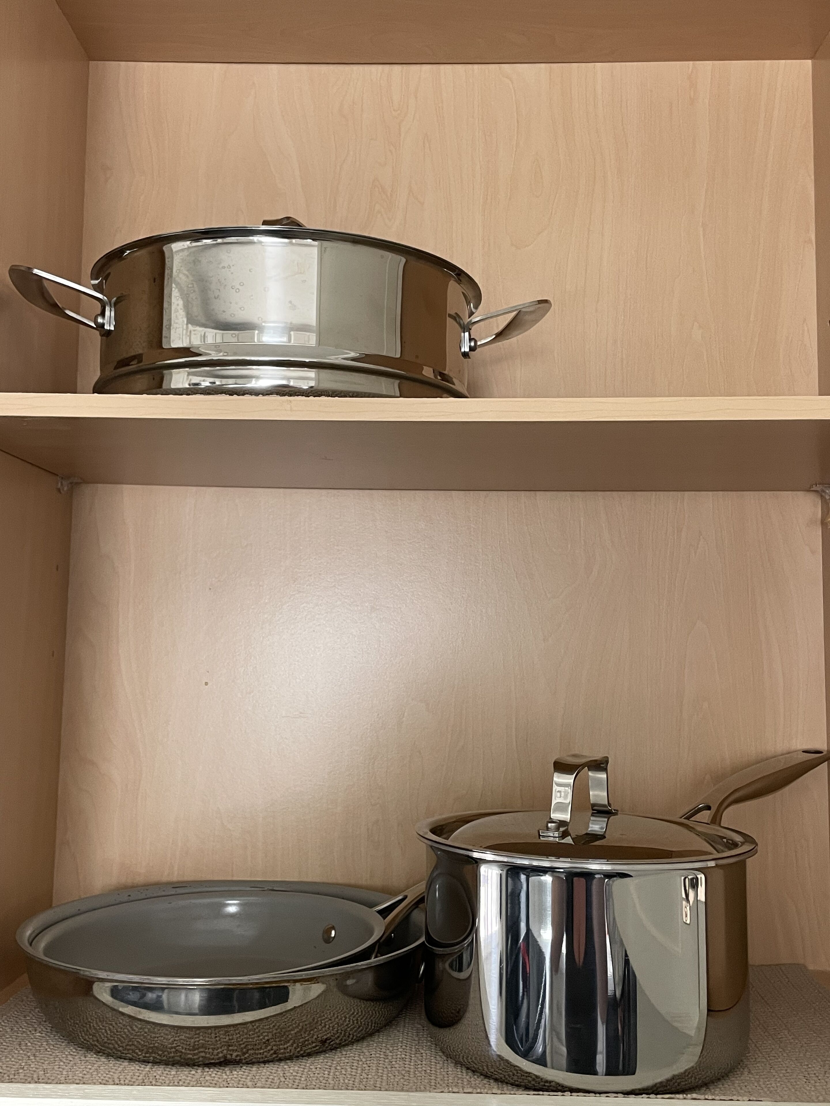 A kitchen with two stainless steel pots on a shelf and countertop.