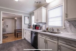 A modern kitchen with white cabinets, a marble countertop, and a dishwasher.